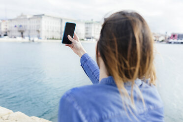 Italien, Triest, junge Frau beim Fotografieren mit dem Handy an der Uferpromenade - BOYF000481