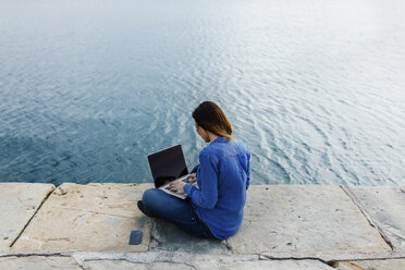 Young woman sitting on dock using laptop - BOYF000482