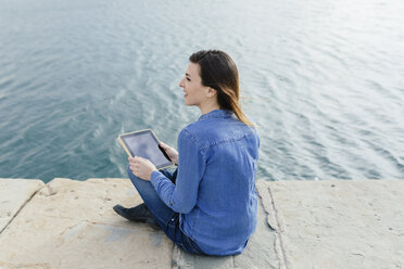 Junge Frau sitzt auf einem Steg und benutzt ein digitales Tablet - BOYF000485