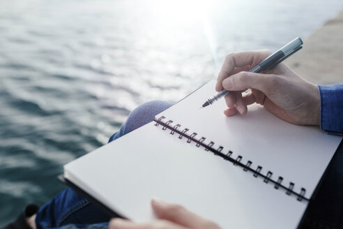 Young woman sitting on dock writing in notebook - BOYF000494