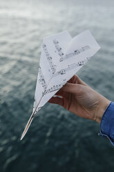 Hand am Wasser, die ein Papierflugzeug aus einem Notenblatt hält - BOYF000505