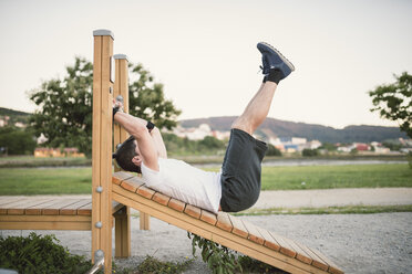 Young man doing sit-ups in a park, outdoors - RAEF001328