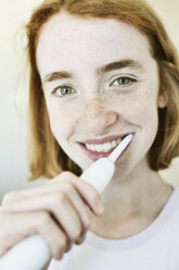 Porträt eines lächelnden Mädchens beim Zähneputzen mit einer elektrischen Zahnbürste - JATF000876