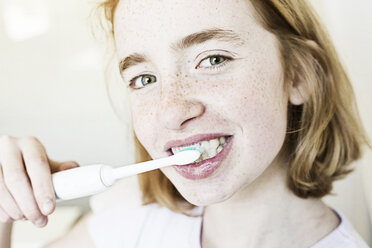 Porträt eines lächelnden Mädchens beim Zähneputzen mit einer elektrischen Zahnbürste - JATF000877