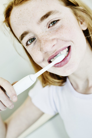 Porträt eines lächelnden Mädchens beim Zähneputzen mit einer elektrischen Zahnbürste, lizenzfreies Stockfoto
