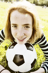 Portrait of smiling girl lying on a meadow with head on soccer ball - JATF000886