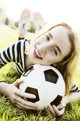 Portrait of smiling girl lying on a meadow with head on soccer ball - JATF000887