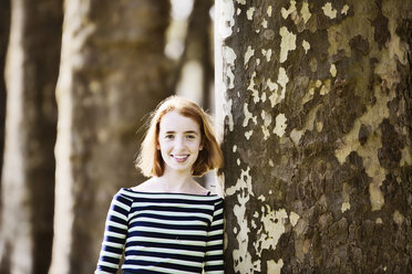 Smiling girl leaning ageinst tree trunk - JATF000888