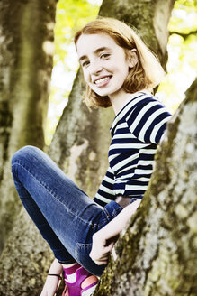 Porträt eines lächelnden Mädchens, das auf einen Baum klettert - JATF000892
