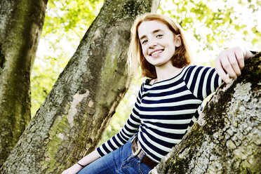 Portrait of smiling girl leaning against tree trunk - JATF000893