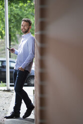 Smiling young man leaning against brick wall - FKF001992