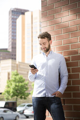 Smiling young man looking at cell phone outdoors - FKF002009