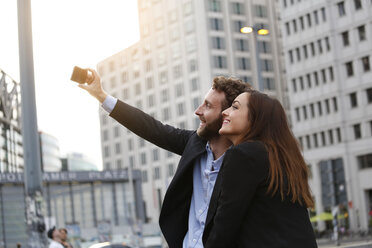 Lächelnder junger Geschäftsmann und Geschäftsfrau nehmen Selfie im Freien - FKF002035