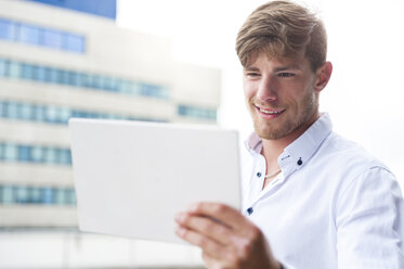 Junger Mann schaut auf ein digitales Tablet im Freien - DIGF000851