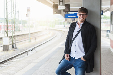 Lächelnder junger Mann wartet am Bahnsteig - DIGF000853