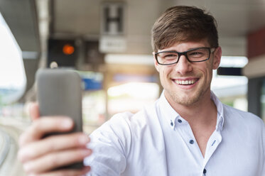 Lächelnder junger Mann auf dem Bahnsteig, der ein Selfie macht - DIGF000856