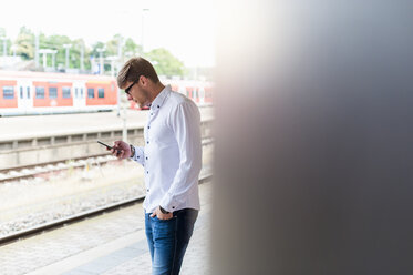 Junger Mann am Bahnsteig schaut auf sein Handy - DIGF000858