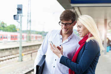 Frau und Mann am Bahnsteig schauen auf ihr Handy - DIGF000862