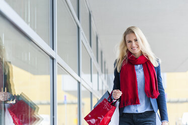 Smiling woman with shopping bags passing urban building - DIGF000866