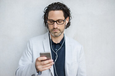 Businessman using smartphone with earphones - DIGF000882