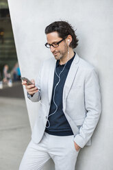 Businessman using smartphone with earphones - DIGF000884