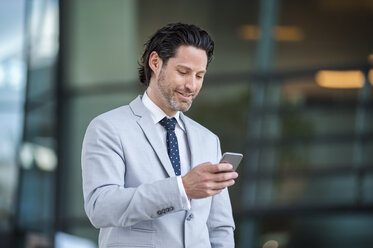 Lächelnder Geschäftsmann schaut auf sein Smartphone - DIGF000908