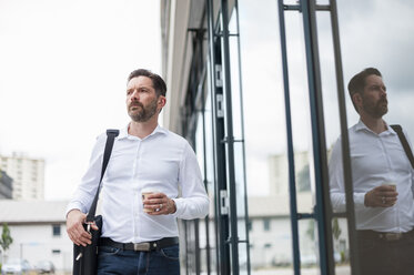 Serious businessman with coffee to go in front of glass facade - DIGF000913