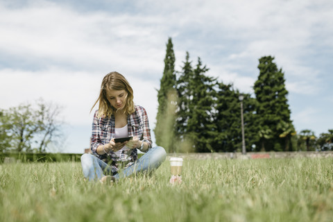 Junge Frau sitzt auf einer Wiese und benutzt ein Mini-Tablet, lizenzfreies Stockfoto