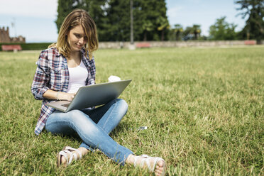 Junge Frau sitzt auf einer Wiese und benutzt einen Laptop - GIOF001366