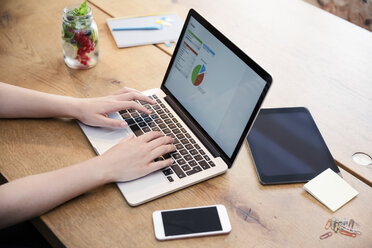 Woman at desk using laptop working on calculation - REAF000094