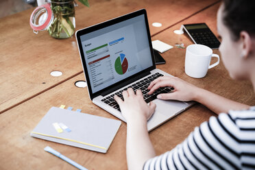 Woman at desk using laptop working on calculation - REAF000095