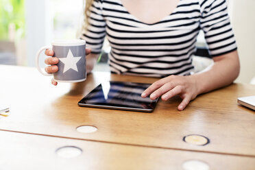 Nahaufnahme einer Frau, die eine Tasse Kaffee hält und ein digitales Tablet benutzt - REAF000106