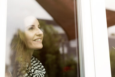 Junge Frau schaut aus dem Fenster, lächelnd - REAF000130