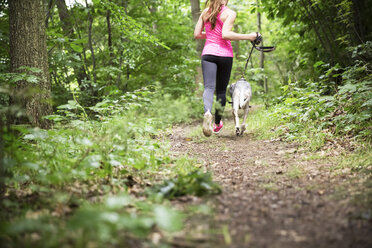 Junge Frau joggt mit Hund im Wald - REAF000145