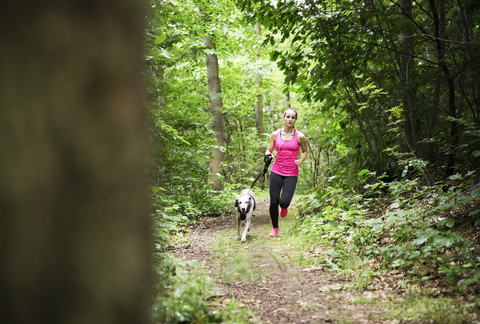 Junge Frau joggt mit Hund im Wald, lizenzfreies Stockfoto