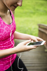 Sportive young woman with smartphone and earbuds - REAF000153
