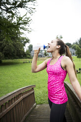 Sportliche junge Frau, die aus einer Flasche trinkt - REAF000158