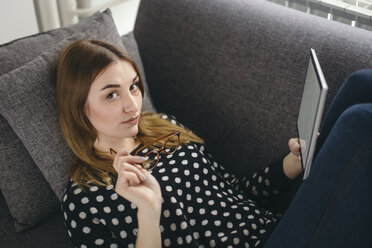 Porträt einer jungen Frau, die sich mit ihrem Tablet auf der Couch entspannt - LCUF000031