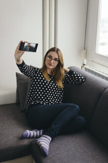 Junge Frau entspannt sich auf der Couch und macht ein Selfie mit ihrem Smartphone - LCUF000032