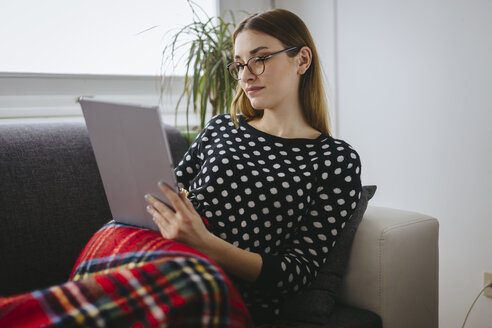 Young woman relaxing on the couch with her tablet - LCUF000033