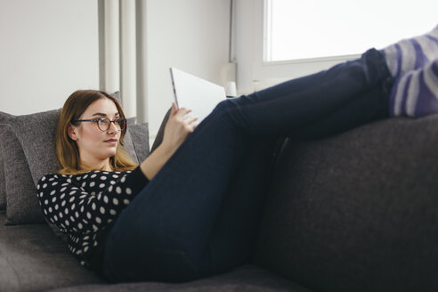 Young woman relaxing on the couch with her tablet - LCUF000034