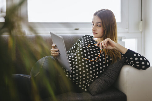 Young woman relaxing on the couch with her tablet - LCUF000035