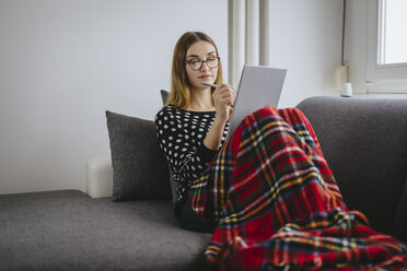 Junge Frau mit Decke zugedeckt entspannt auf der Couch mit ihrem Tablet - LCUF000036