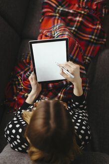 Junge Frau entspannt sich auf einer Couch und zeichnet mit einem Stift auf einem Tablet, Ansicht von oben - LCUF000037