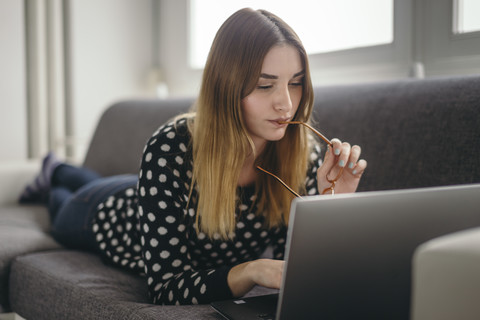 Junge Frau entspannt auf der Couch mit Laptop, lizenzfreies Stockfoto