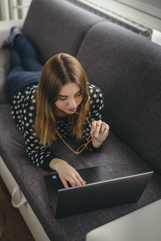 Junge Frau entspannt auf der Couch mit Laptop, lizenzfreies Stockfoto