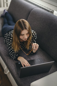 Young woman relaxing on the couch using laptop - LCUF000039