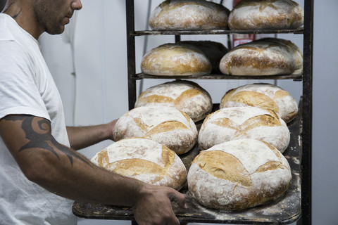 Bäcker legt ein Tablett mit Brot in einer Bäckerei, lizenzfreies Stockfoto