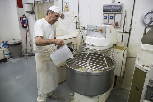 Bäcker gießt Wasser in eine industrielle Knetmaschine - ABZF000922