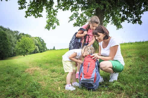 Mother and daughters on meadow during hiking, looking into backpack - VTF000548